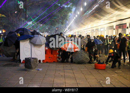 11 agosto 2019 Hong Kong. Manifestanti tenendo il coperchio dietro barricate e ombrelloni come fuoco di polizia gas lacrimogeni e pallottole di gomma da Tsim Sha Tsui stazione di polizia durante un anti extradition bill protesta. Foto Stock