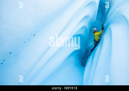 Arrampicata su ghiaccio una caverna di ghiaccio sul ghiacciaio Matanuska, un uomo bashes scaglie di ghiaccio come egli oscilla per il suo strumento nella parete a salire. Foto Stock