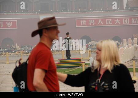 I turisti stranieri a piedi passato un poliziotto paramilitari di guardia sulla piazza Tiananmen in pesanti smog a Pechino, in Cina, il 9 ottobre 2014. Pechino Foto Stock