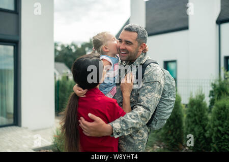 Uomo militare abbracciando la moglie e la figlia dopo il ritorno a casa Foto Stock