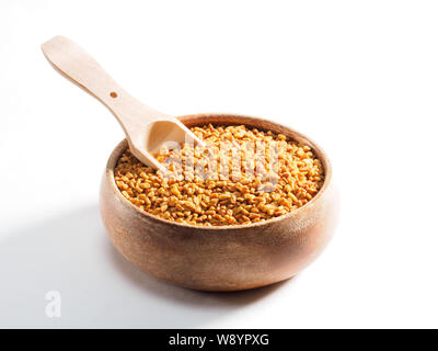 Fenugreek (Trigonella) in una coppa di legno con uno scoop su sfondo bianco Foto Stock