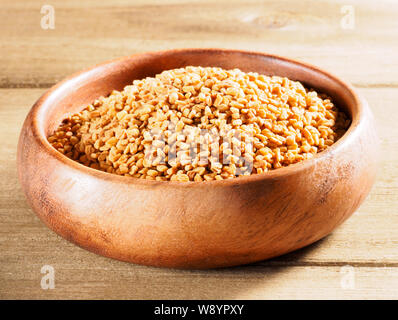 Fenugreek (Trigonella) in una coppa di legno su un sfondo di legno Foto Stock