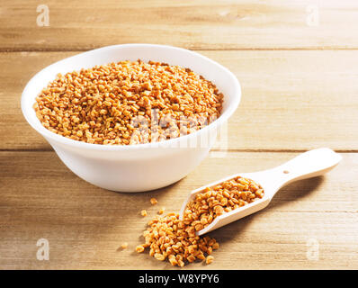 Fenugreek (Trigonella) in una ceramica tazza bianca con scoop su uno sfondo di legno Foto Stock