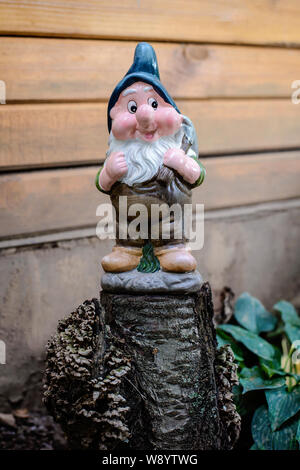 Figurina di un divertente nana in giardino su un moncone su uno sfondo di legno Foto Stock