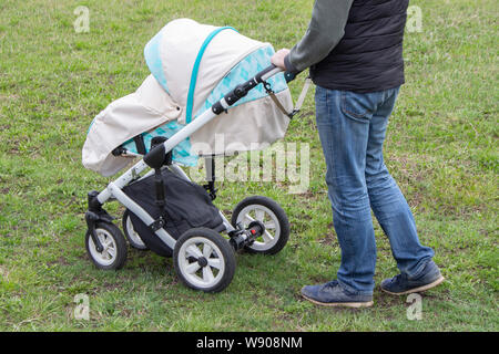 Il padre le passeggiate con il carrello,vista dal basso solo le gambe. Luminose passeggino di menta e gambe in jeans, passeggiate con il bambino in natura outdoor. Un uomo in jeans e Foto Stock