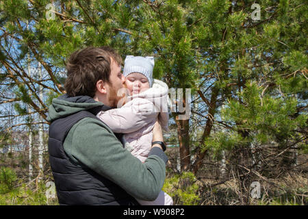 Un giovane padre baci un neonato figlia, una passeggiata nel parco un papà con una bambina tenerezza amore care, un genitore amorevole ritratto di famiglia Foto Stock