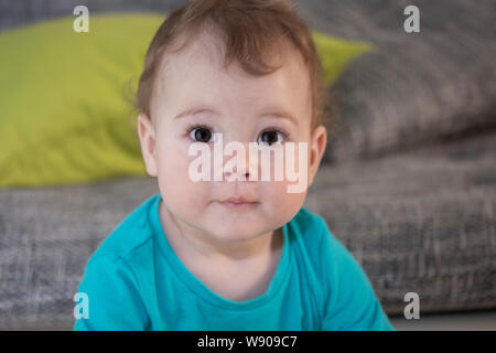 Ritratto di un simpatico sorpreso toddler ragazza ragazzo di 10 mesi. Il Bambino guarda con gli occhi sorpreso. Un bambino in una maglietta blu, un grande ritratto di una divertente surpr Foto Stock