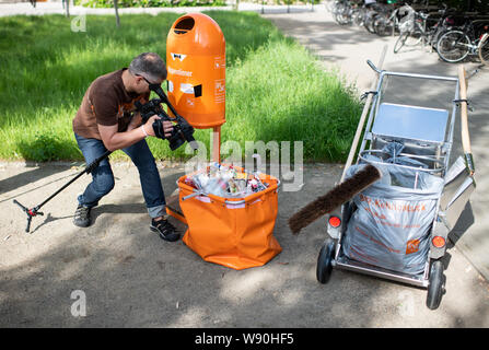 Berlino, Germania. 12 Ago, 2019. Un cameraman pellicole il contenuto di una tipica strada bidone dei rifiuti con numerosi pacchetti, tazze monouso e rifiuti residui in occasione di una conferenza stampa dal titolo "città pulita e più la responsabilità del produttore per i prodotti monouso' sulla possibilità di sostenere lo smaltimento dei rifiuti nel cortile della Federal Ministero dell'ambiente. I produttori di articoli monouso come mozziconi di sigaretta e monouso Tazze di caffè sono a condividere i costi della pulizia municipale in futuro. Credito: Bernd von Jutrczenka/dpa/Alamy Live News Foto Stock