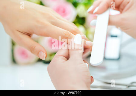 Le mani di un qualificato manicurist il deposito delle unghie di una giovane donna Foto Stock