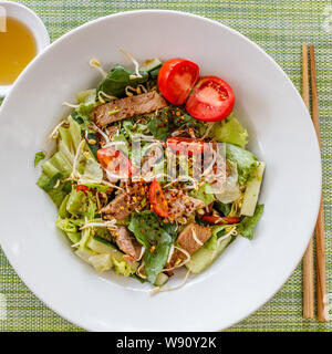 Il filato Nuea Yang o insalata di carne tailandese - cucina tradizionale della Thailandia. Salsa a lato. Su sfondo verde. Foto Stock