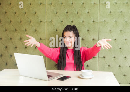 Felice di vedere voi! Incantevole romantico lieto giovane ragazza freelancer nero con dreadlocks acconciatura seduto da solo e pronto abbracciando con bracci sollevati, troppo Foto Stock