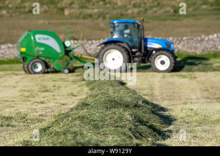 Rendendo haylage raccolto su una collina fattoria, con un New Holland T6030 e un McHale 5500 imballatrice. Cumbria, Regno Unito. Foto Stock