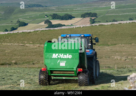 Rendendo haylage raccolto su una collina fattoria, con un New Holland T6030 e un McHale 5500 imballatrice. Cumbria, Regno Unito. Foto Stock