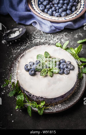 Mirtillo n. cuocere vegan cheesecake con latte di cocco , decorate con mirtilli freschi e foglie di menta su scuro dello sfondo rustico Foto Stock