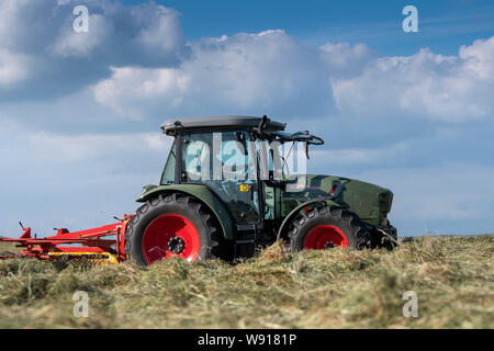 Agricoltore remare fino al fieno con un trattore Hurlimann e a due pass rastrello su una collina di pennini agriturismo vicino a Ravenstondeale, Cumbria. Foto Stock