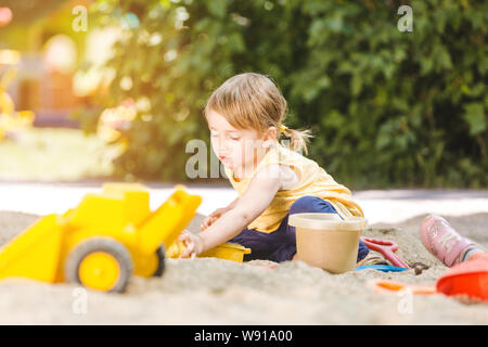 Bambina avente un sacco di divertimento con i suoi giocattoli giocando nella sandbox Foto Stock