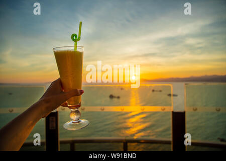 Mano che trattiene il vetro tazza di succo di mango nel bel tramonto sfondo, Cina Foto Stock