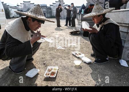 --FILE--extra cinese mangiare come essi squat sul terreno a pranzo durante una sessione di riprese di una serie TV al mondo Hengdian Studios di Dongyang city Foto Stock