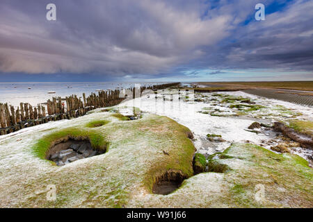 Un paesaggio invernale del Waddensea nei Paesi Bassi con le nuvole scure in background e la neve sulla riva - Moddergat, Paesi Bassi Foto Stock