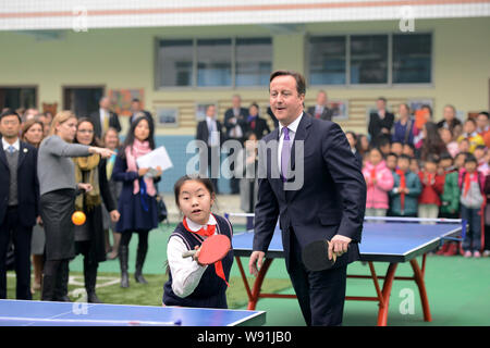 Primo Ministro britannico David Cameron, diritto, gioca a tennis da tavolo con giovani studenti cinesi durante la sua visita ad una scuola elementare nella città di Chengdu, sout Foto Stock