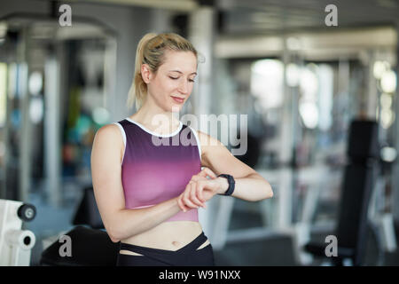 Donna che guarda la smart indossabile a guardare mentre esercizio presso il centro fitness Foto Stock