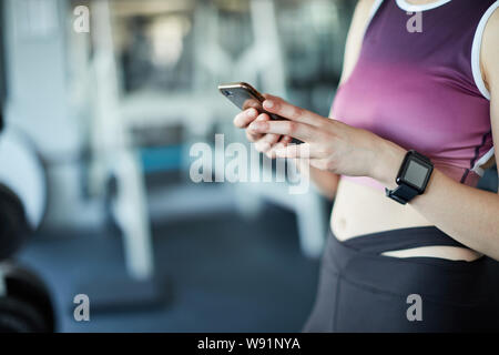 Donna che utilizza smartphone e smart watch indossabile in palestra mentre ti alleni Foto Stock