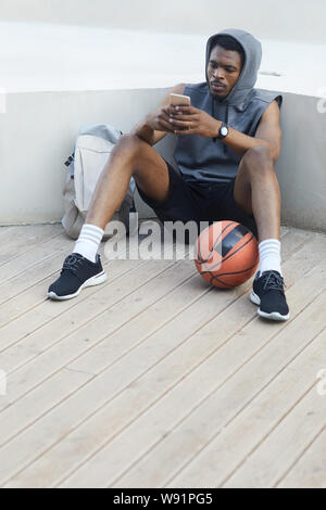 A piena lunghezza Ritratto di contemporaneo afro-uomo utilizza lo smartphone durante i momenti di relax nel parco all'aperto, spazio di copia Foto Stock