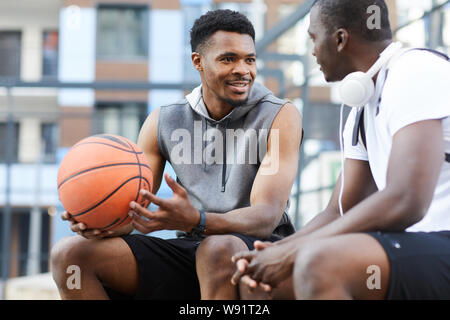 Ritratto di due ragazzi afroamericani chiacchierando seduti sul campo da basket all'aperto, spazio di copia Foto Stock