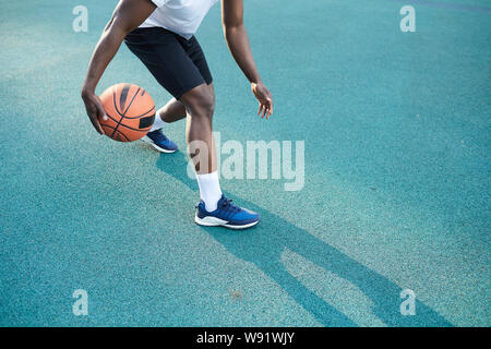 Angolo basso azione girato di afro-americano di uomo giocare a basket all'aperto, spazio di copia Foto Stock