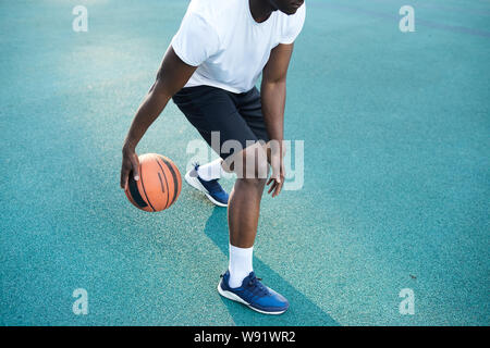 Azione girato di un irriconoscibile uomo africano giocare a basket all'aperto, spazio di copia Foto Stock