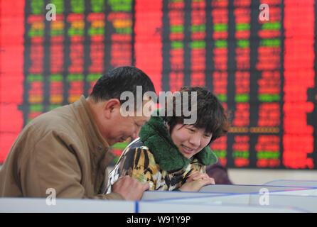 Due investitori cinesi sono felicemente sorridere quando il controllo dei prezzi delle azioni (rosso per il prezzo in salita) in corrispondenza di un magazzino casa di brokeraggio in città Fuyang, est Chinas Foto Stock