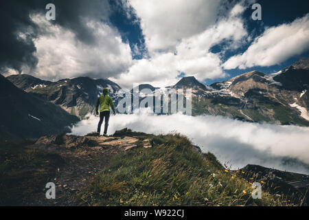 Ampio panorama di montagna. Piccole silhouette di persona sulla montagna rocciosa pendio coperto con il bianco puffy nuvole e nebbia. Foto Stock