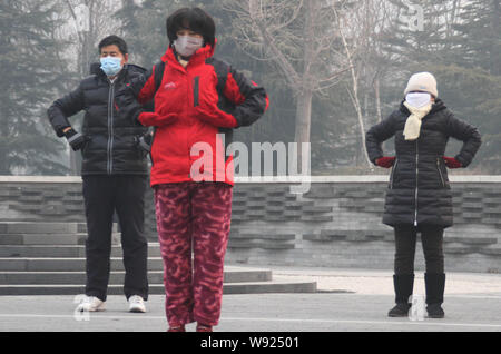 Cinesi locali residenti indossano maschere viso fare esercizi del mattino al Parco Lishuiqiao in pesanti smog a Pechino, in Cina, il 25 dicembre 2013. Pechino risiedono Foto Stock