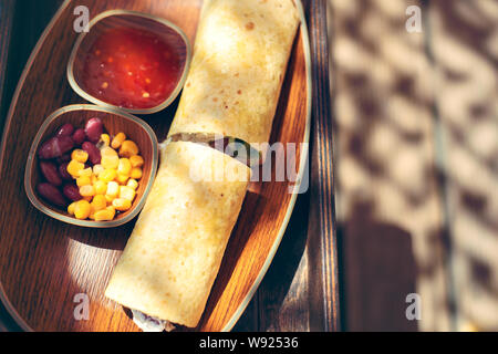 Burrito si avvolge con carne, legumi e verdure sul pannello di legno. Foto Stock