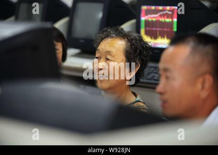 Un investitore cinese sorride come guarda i prezzi delle azioni e indici di borsa a uno stock brokerage house di Qingdao City East Chinas provincia di Shandong Foto Stock