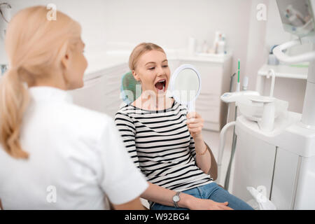 Dentisti paziente guardando i suoi denti nello specchio. Foto Stock