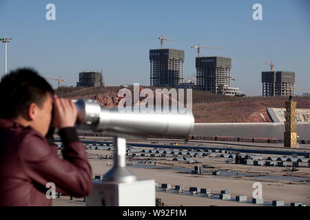 --FILE--un uomo utilizza un telescopio per guardare i nuovi edifici in costruzione nel quartiere Kangbashi, Ordos city, porcellane del nord della Mongolia Interna Reg autonoma Foto Stock