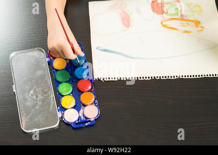 Dettaglio di un bambino con le mani in mano tenendo un pennello e pittura con acquarello su carta. Concetti di infanzia, educazione e il ritorno a scuola. Foto Stock