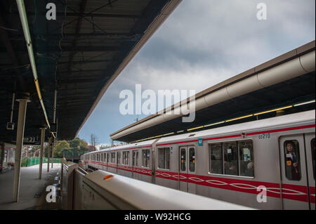 Tokyo, Giappone - Aprile 2019: il bianco e il rosso giapponese treno dei pendolari in una stazione ferroviaria. Vista lungo la piattaforma con la nuvola grigio cielo di sfondo Foto Stock