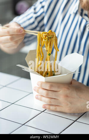 Close-up di un giovane uomo non identificato la mano in una camicia di contenimento sono bastoncini di legno a base di noodle cinesi. Deliziosa cucina asiatica concetto. Foto Stock