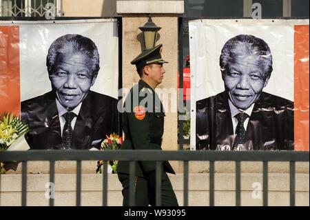 Un Cinese di paramilitari poliziotto passeggiate passato foto dell ex presidente sudafricano Nelson Mandela che viene visualizzata al South African Embassy in ch Foto Stock