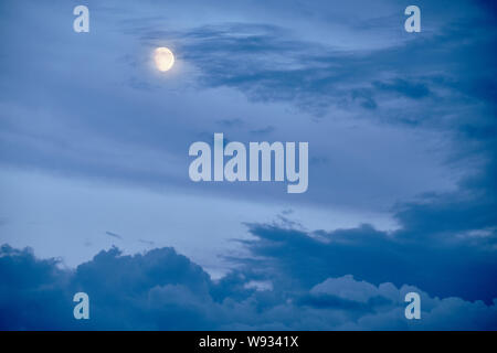 La luna si nasconde dietro alcune nuvole su un drammatico cielo di sera in estate in Germania Foto Stock