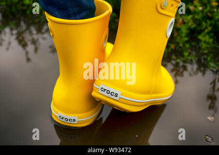 Tambov, Federazione Russa - Agosto 08, 2019 Donne gambe in giallo Crocs stivali nella pozza. Foto Stock