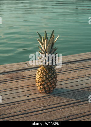 Un ananas su un deck e un'acqua turchese in background. Foto Stock