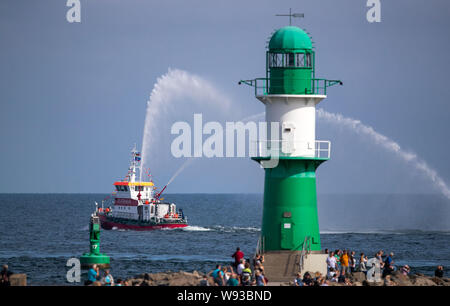 09 agosto 2019, Meclemburgo-Pomerania, Rostock-Warnemünde: il secondo giorno della ventinovesima Hanse Sail una squadra di vigili del fuoco barca schizzi fontane d'acqua di fronte al molo luce a Warnemünde all'inizio della gita in barca a vela sul Mar Baltico. Fino al 11.08.2019, 170 navi e circa un milione di visitatori sono attesi alla Quattro giorni di fiera marittima. Foto: Jens Büttner/dpa-Zentralbild/ZB Foto Stock