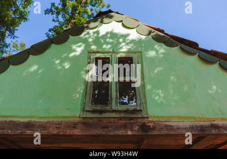 L'esterno di una vecchia casa in legno, dettagli di piccolo soppalco finestra e tetto verde. Foto Stock