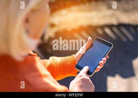 Donna bionda utilizzando reti sociali, orologi video sul telefono sulla giornata di sole Foto Stock