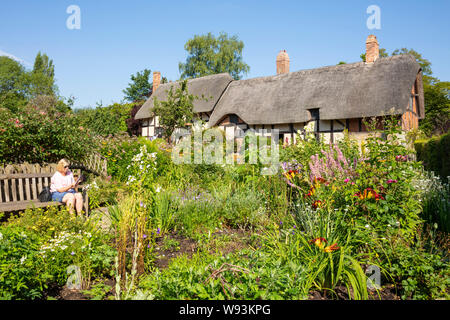 Anne Hathaway cottage un cottage in paglia in un giardino cottage con donna seduto su una panca Shottery vicino Stratford upon Avon Warwickshire Inghilterra GB Foto Stock