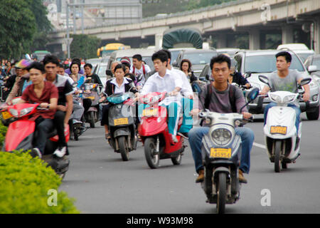 I ciclisti cinese di guidare la propria bici elettriche o scooter su una strada nel centro della città di Haikou, sud Chinas Hainan provincia, 15 marzo 2013. Foto Stock