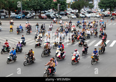 I ciclisti cinese di guidare la propria moto, bici elettriche o scooter su una strada nel centro della città di Haikou, sud Chinas Hainan provincia, 15 marzo 2013. Foto Stock